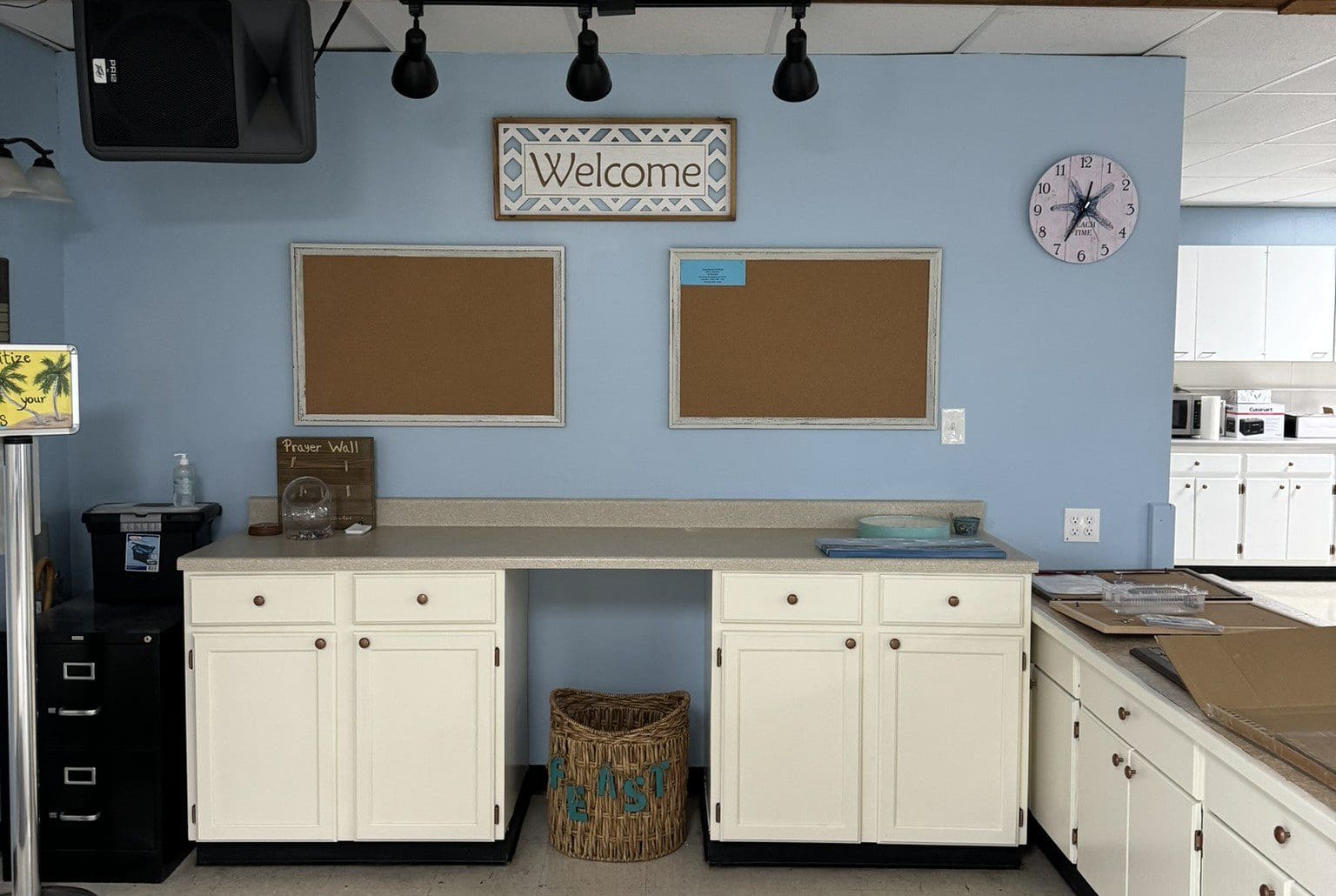 Organized classroom corner with white cabinets, bulletin boards, and a welcome sign.